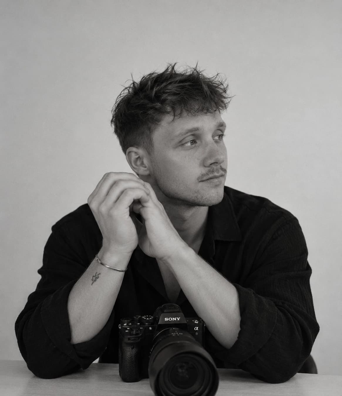 Zwart-witportret van Noah Ubert aan tafel, met zijn camera voor zich